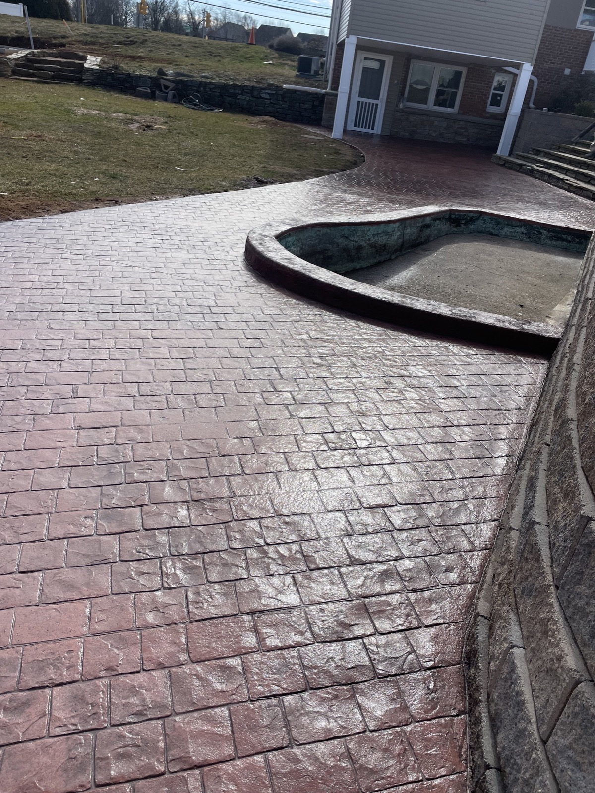 Burgundy stamped concrete driveway with retaining wall and pool